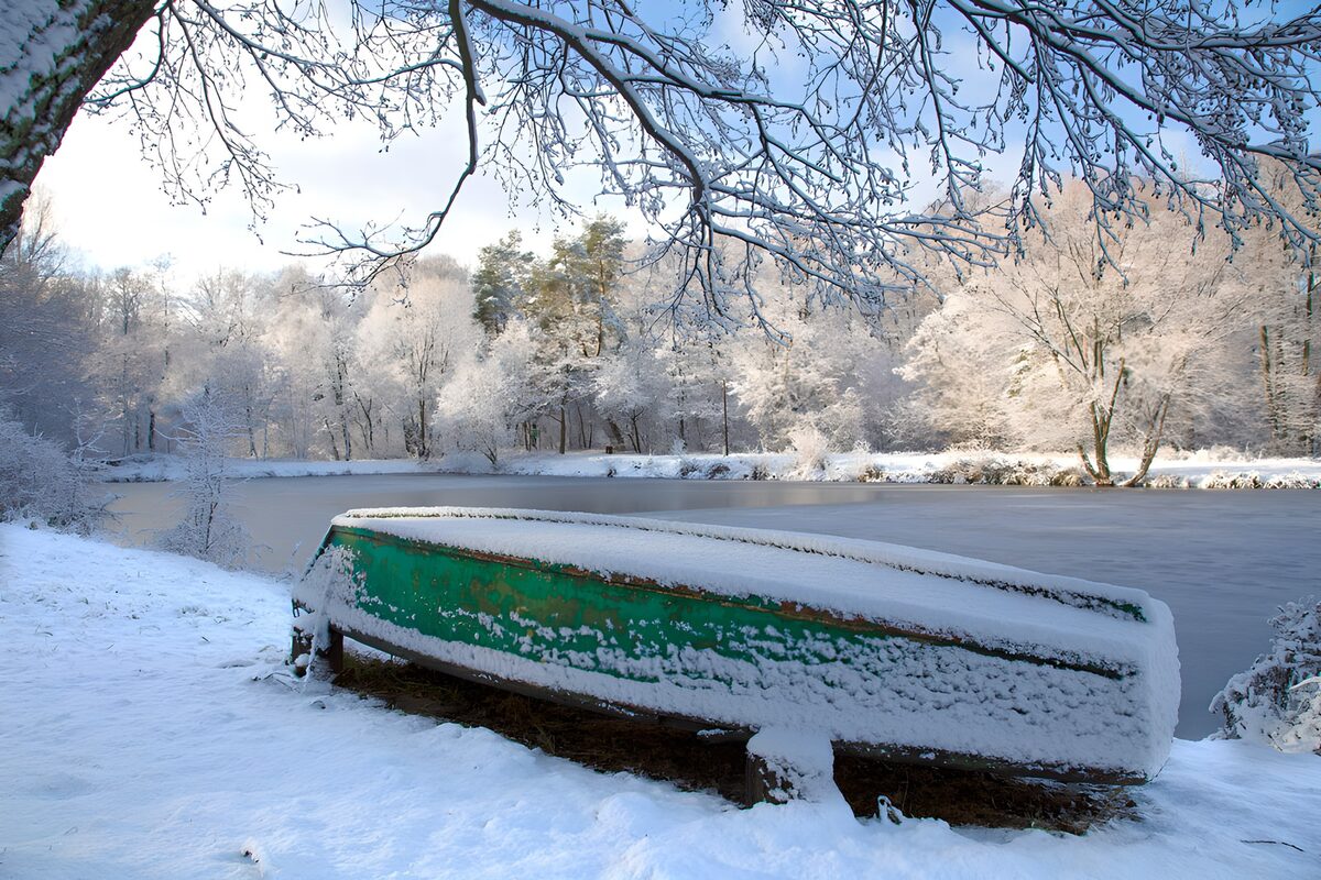 Snow-covered green boat by a frozen pond