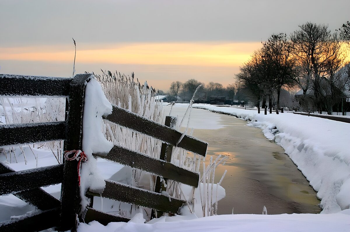 Snowy fence by a frozen canal at dusk