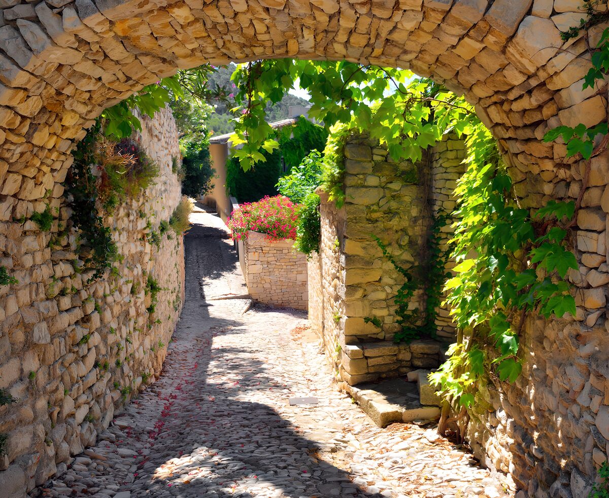 Sunlit cobbled lane through a stone arch