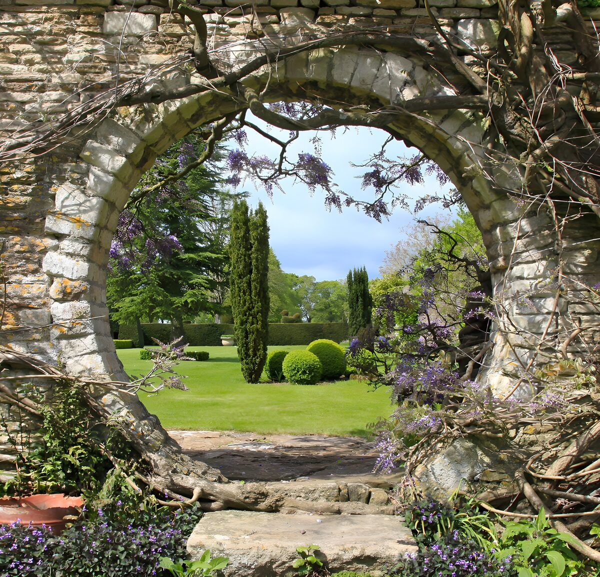 Sunlit garden through a flowered stone arch