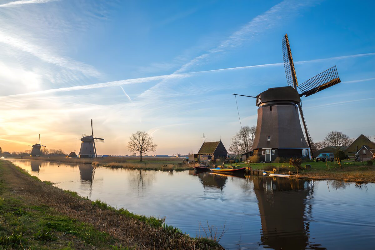 Three windmills beside a canal at sunset