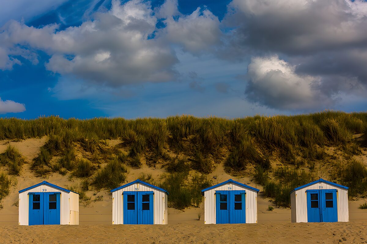 Four blue-doored beach huts on golden sand