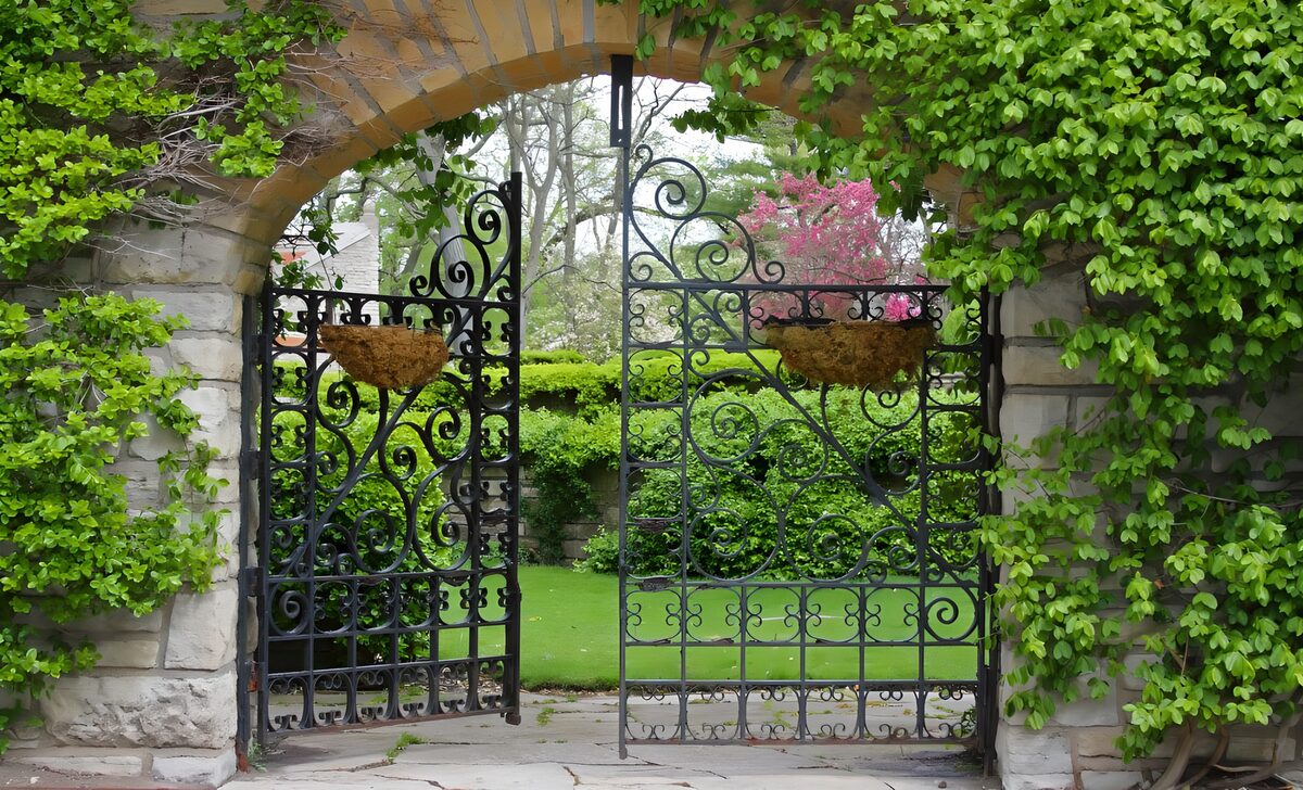 Open wrought iron gate under a leafy arch