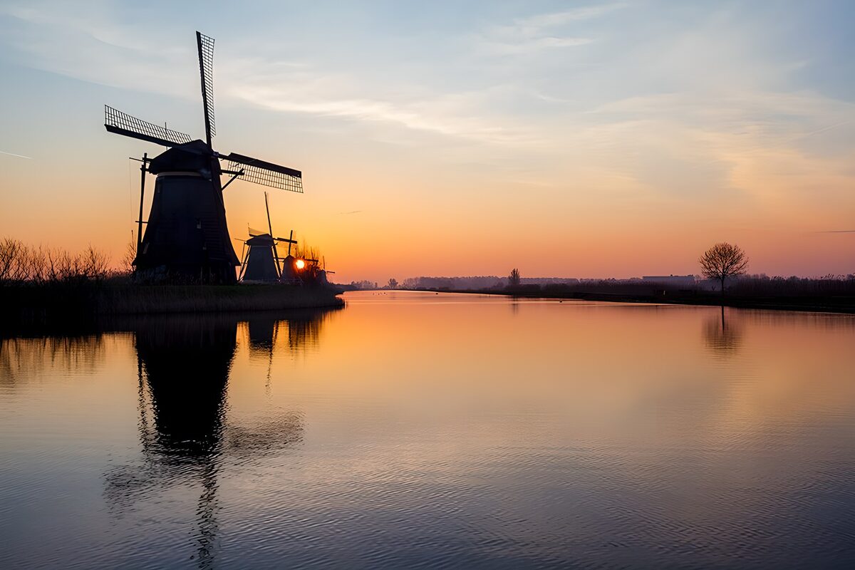Windmills by calm water at sunset