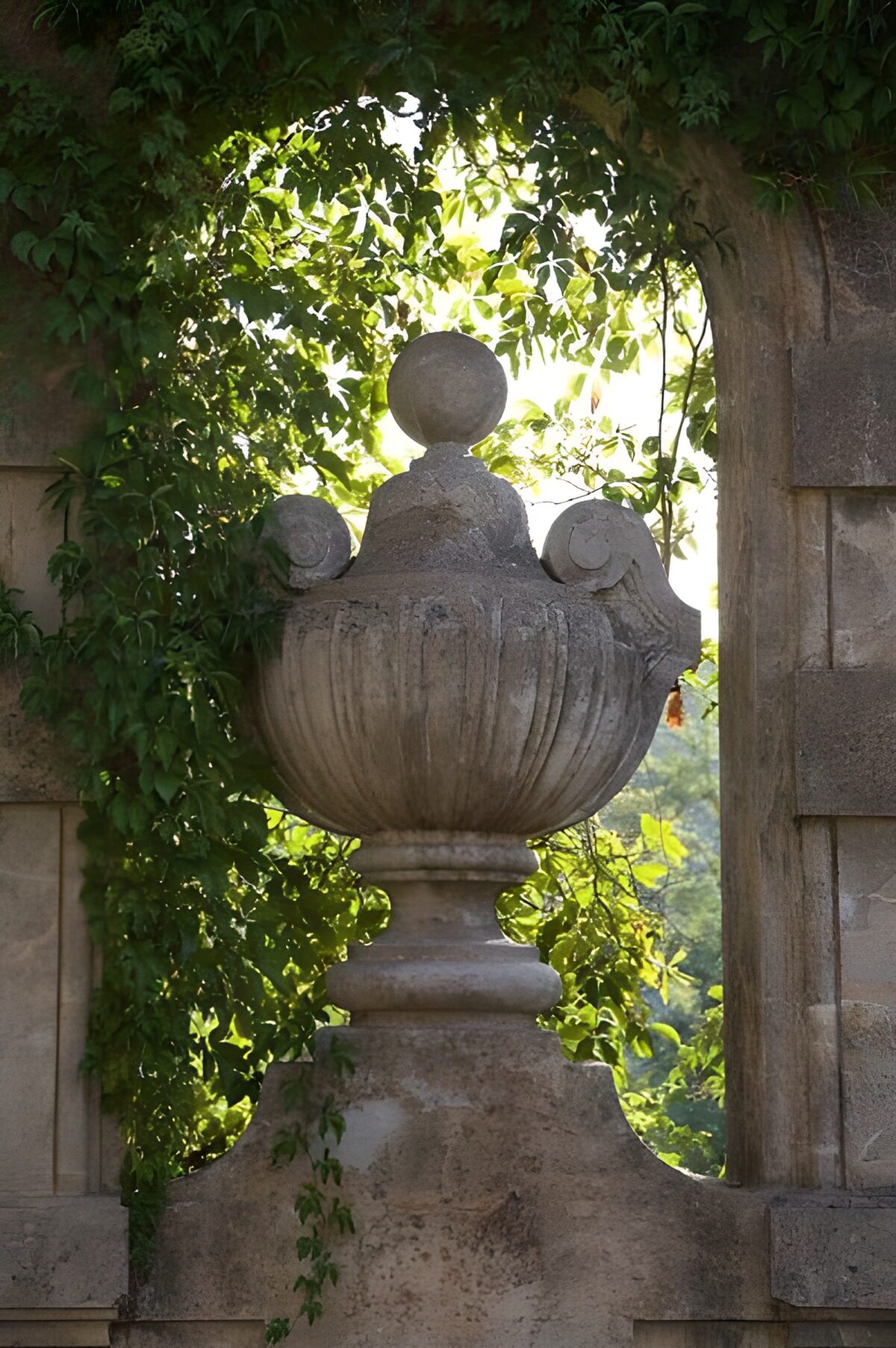 Weathered stone urn beneath a leafy arch