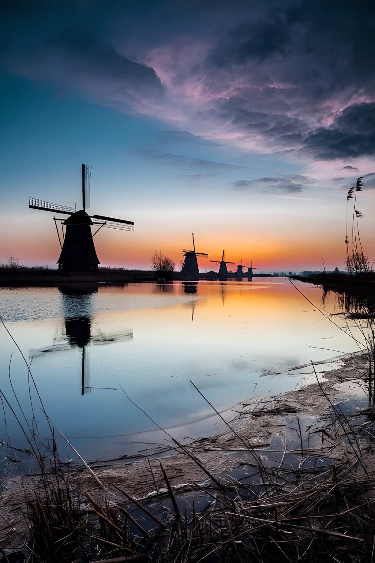 Windmills by still water at sunset