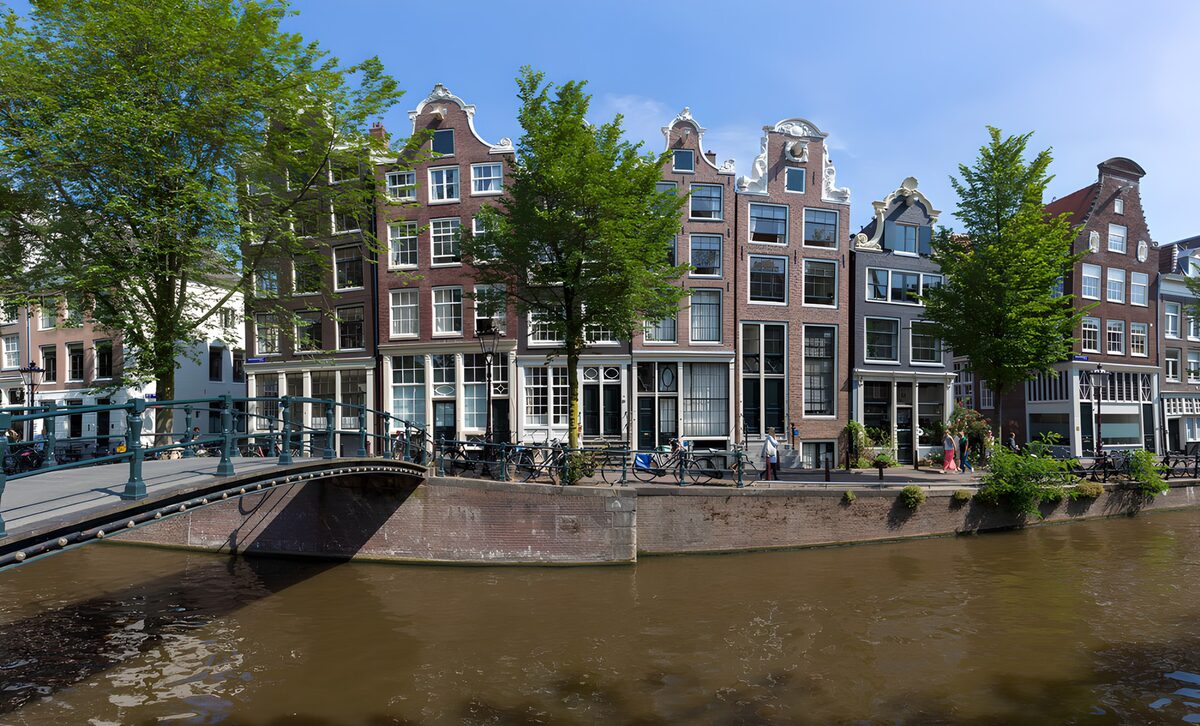 Sunlit canal houses and a leafy quay