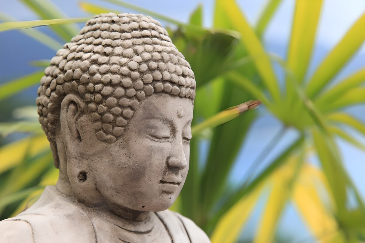 Pale grey Buddha against green leaves