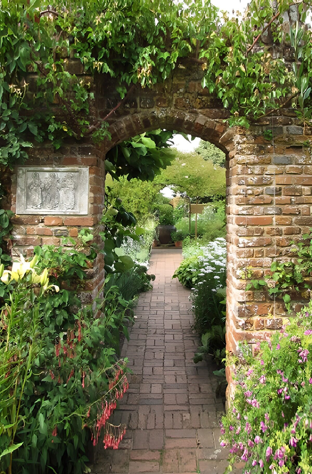Flower-lined path beneath an old brick arch