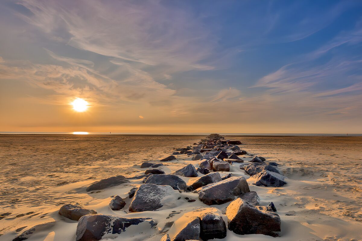 Sunset over sand and a rocky breakwater