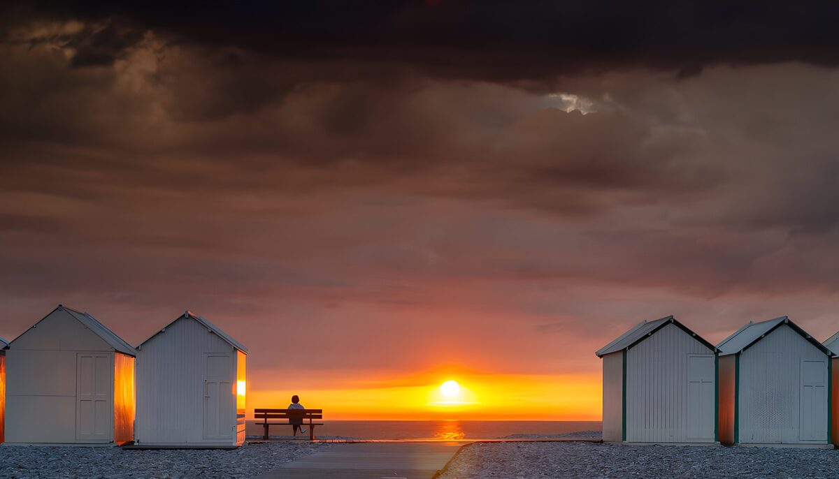 White beach huts under a dramatic sunset
