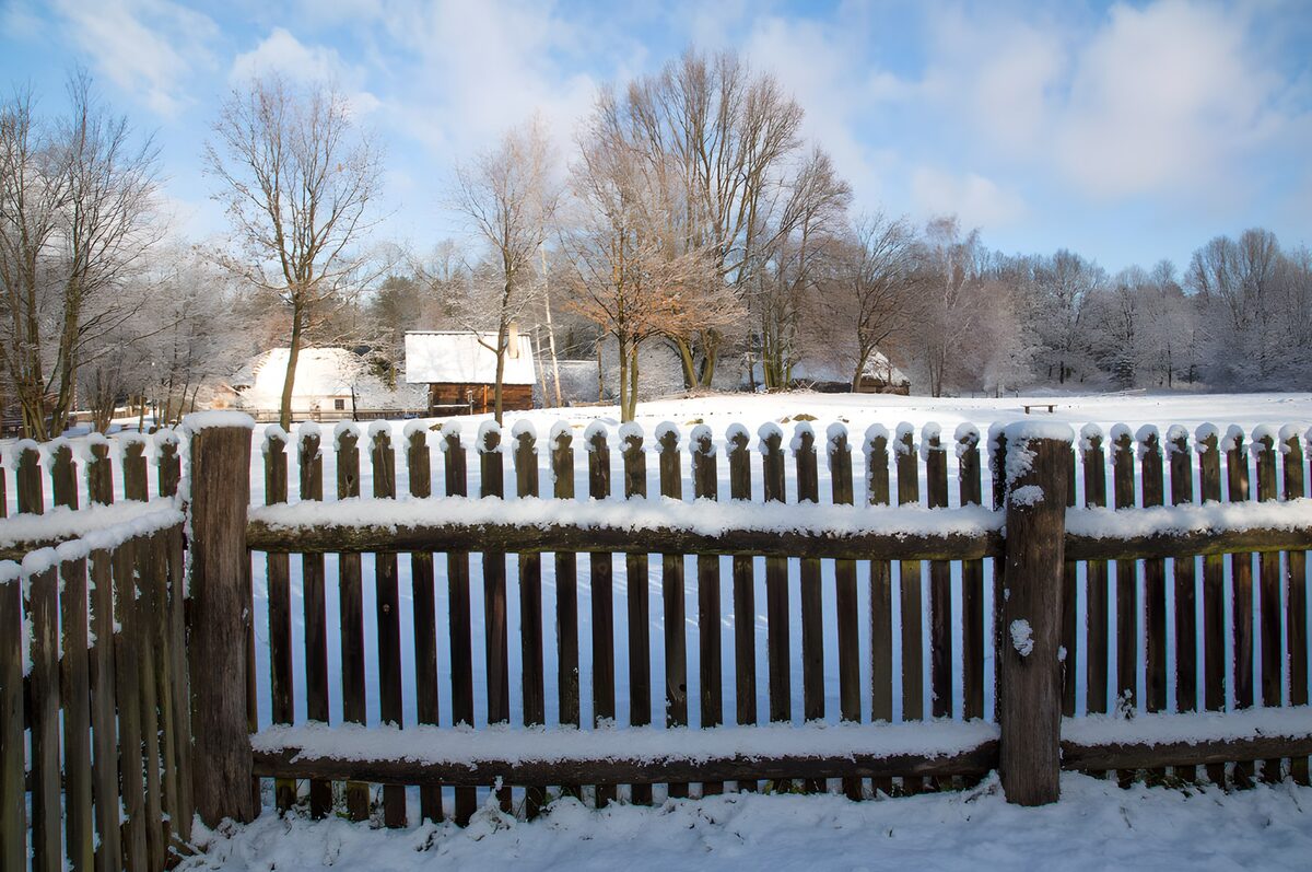 Snow-covered fence and rural buildings